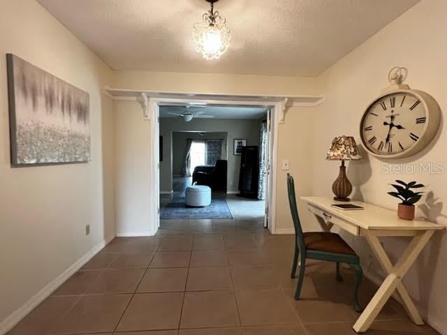 hallway with baseboards, a textured ceiling, and tile patterned floors