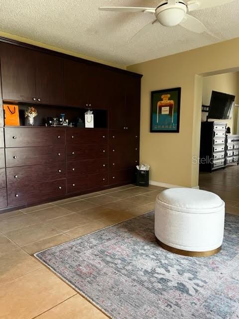 interior space with ceiling fan, a textured ceiling, baseboards, and tile patterned floors