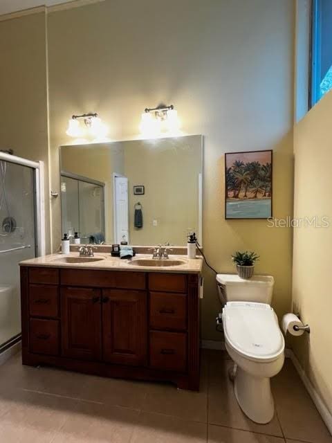 bathroom featuring toilet, a sink, a shower stall, tile patterned floors, and double vanity