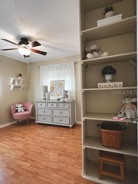 interior space featuring a ceiling fan, baseboards, a textured ceiling, and light wood finished floors