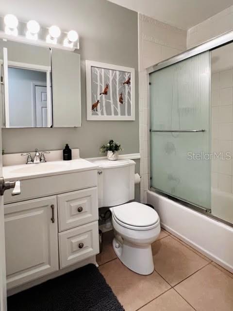 bathroom with combined bath / shower with glass door, vanity, toilet, and tile patterned floors