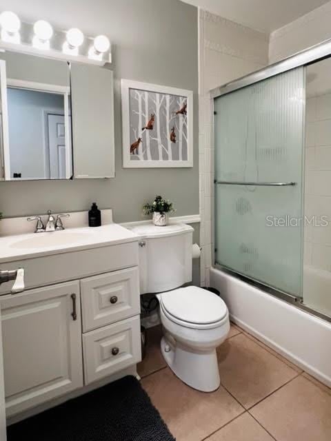 full bath with toilet, shower / bath combination with glass door, tile patterned flooring, and vanity