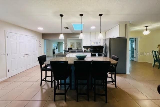 kitchen featuring light tile patterned floors, electric stove, white microwave, and freestanding refrigerator