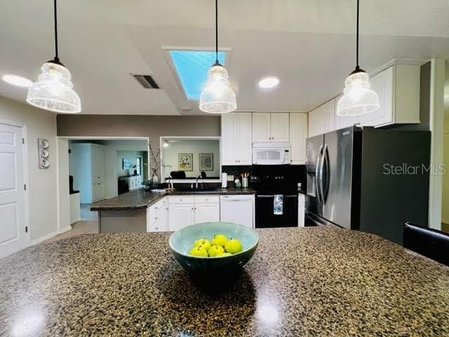 kitchen with a peninsula, white appliances, a sink, visible vents, and white cabinetry