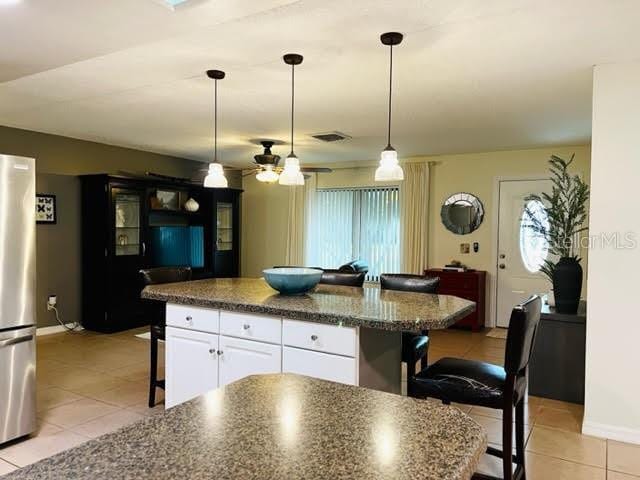 kitchen with light tile patterned floors, visible vents, freestanding refrigerator, a kitchen bar, and white cabinetry