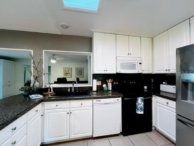 kitchen with light tile patterned floors, white cabinetry, a sink, dark stone countertops, and white appliances