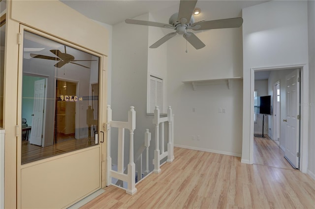 unfurnished room with ceiling fan, a towering ceiling, and light wood-type flooring