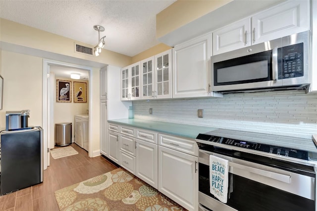 kitchen featuring appliances with stainless steel finishes, separate washer and dryer, white cabinets, decorative backsplash, and a textured ceiling