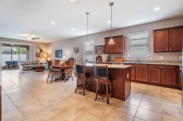 kitchen with a center island, hanging light fixtures, a kitchen breakfast bar, ceiling fan, and light stone countertops