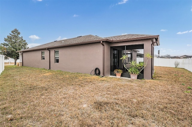 rear view of property with a yard, fence, a sunroom, and stucco siding