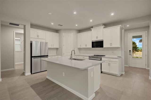 kitchen with appliances with stainless steel finishes, sink, white cabinets, decorative backsplash, and a kitchen island with sink