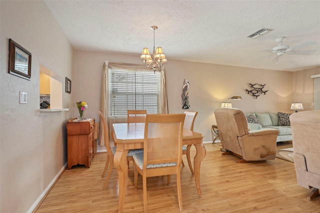 dining area with ceiling fan with notable chandelier, a textured ceiling, and light hardwood / wood-style floors