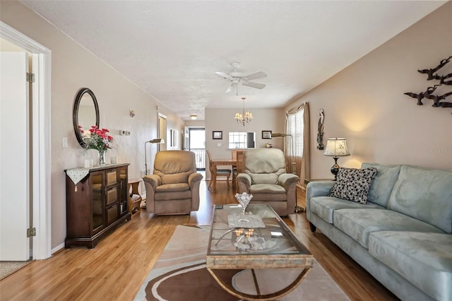 living room with ceiling fan with notable chandelier, a textured ceiling, and light hardwood / wood-style flooring