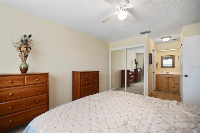 carpeted bedroom featuring a textured ceiling, a closet, ceiling fan, and ensuite bathroom