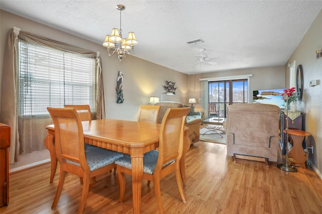 dining area with ceiling fan with notable chandelier, a textured ceiling, and light wood-type flooring