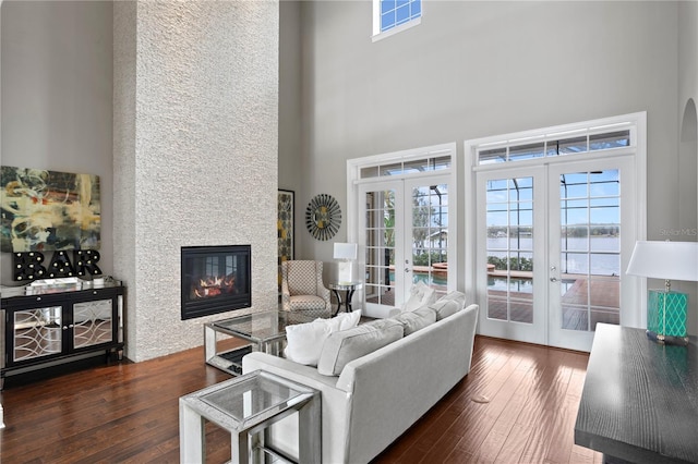 living room featuring french doors, a water view, a large fireplace, dark hardwood / wood-style floors, and a towering ceiling