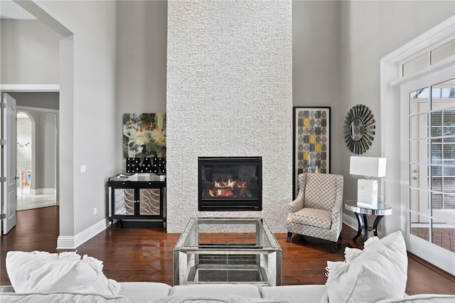 living room with dark wood-type flooring, a fireplace, and a towering ceiling