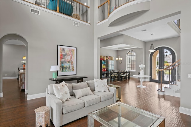 living room featuring dark wood-type flooring, an inviting chandelier, and a towering ceiling