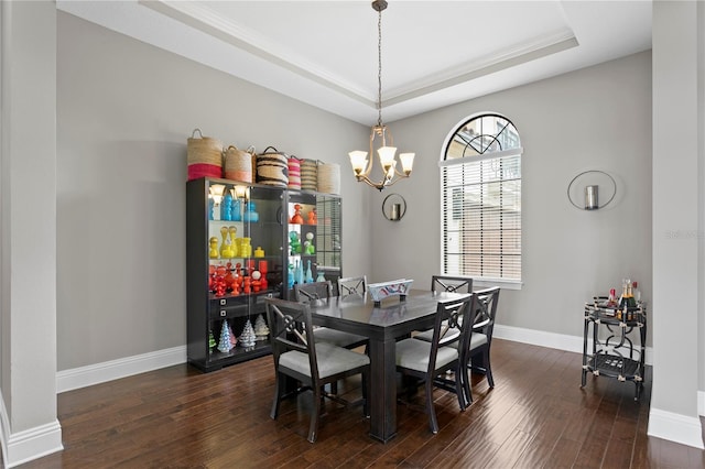 dining space with a raised ceiling, dark wood-type flooring, and a chandelier