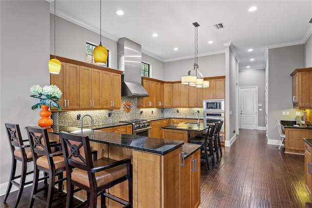 kitchen with appliances with stainless steel finishes, sink, a kitchen breakfast bar, hanging light fixtures, and wall chimney exhaust hood