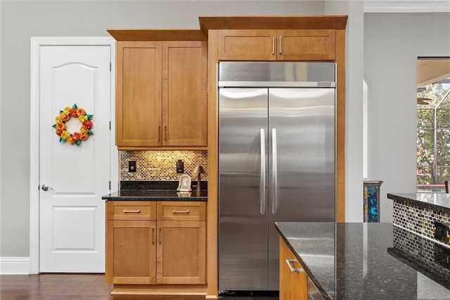 kitchen featuring stainless steel built in fridge, backsplash, dark hardwood / wood-style floors, and dark stone counters