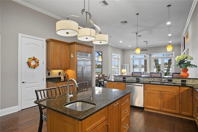 kitchen featuring appliances with stainless steel finishes, sink, a kitchen island with sink, and dark stone counters