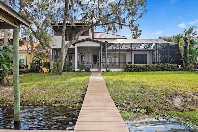 back of property featuring a water view, a balcony, glass enclosure, and a lawn