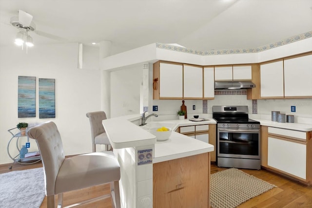 kitchen featuring electric stove, sink, a kitchen breakfast bar, kitchen peninsula, and light hardwood / wood-style flooring