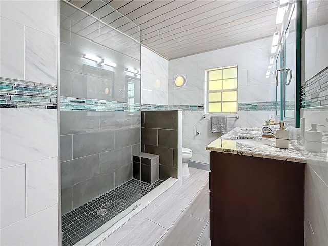 bathroom with a shower with door, vanity, tile walls, and toilet