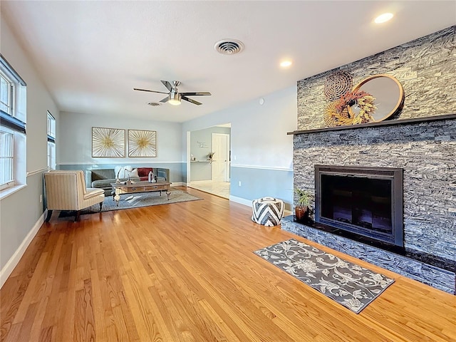 living room with hardwood / wood-style flooring, ceiling fan, and a stone fireplace