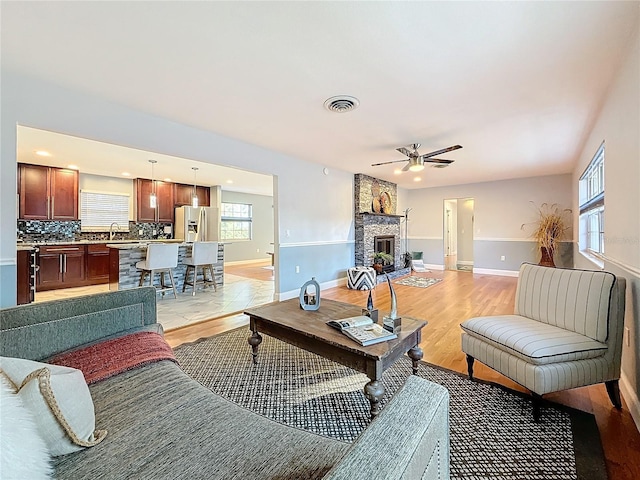 living room featuring ceiling fan, a stone fireplace, sink, and light wood-type flooring