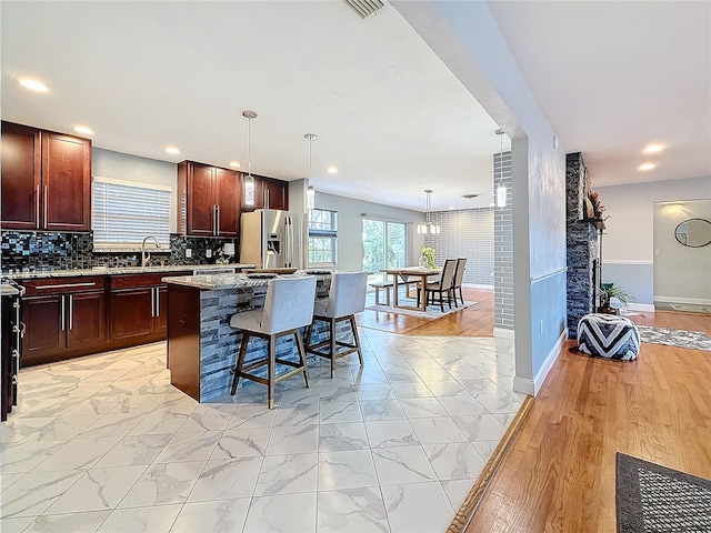 kitchen with a kitchen breakfast bar, stainless steel refrigerator with ice dispenser, decorative backsplash, a kitchen island, and decorative light fixtures