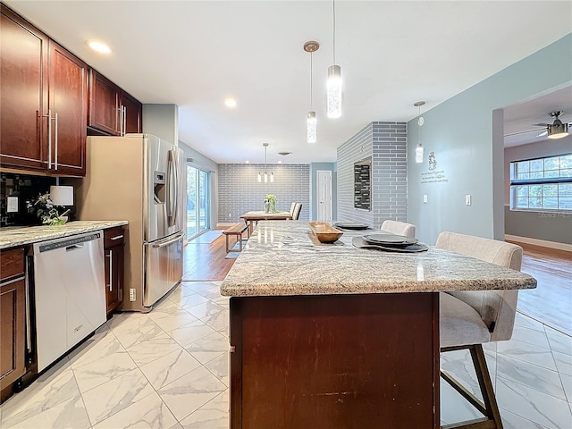 kitchen featuring hanging light fixtures, stainless steel appliances, light stone countertops, a kitchen bar, and decorative backsplash