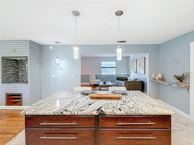 kitchen featuring a kitchen island, a fireplace, light stone counters, and decorative light fixtures