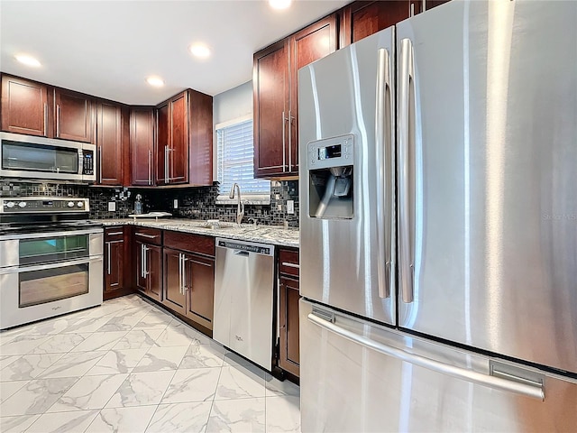 kitchen featuring light stone counters, backsplash, stainless steel appliances, and sink