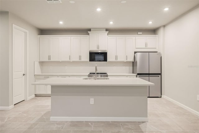 kitchen featuring a kitchen island with sink, white cabinetry, and stainless steel refrigerator