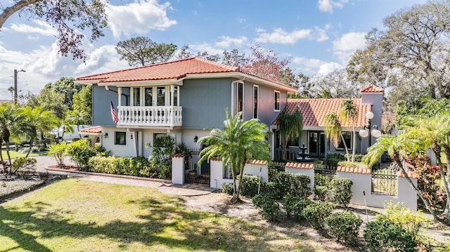 view of front of property with a fenced front yard, a front yard, a tile roof, and a balcony