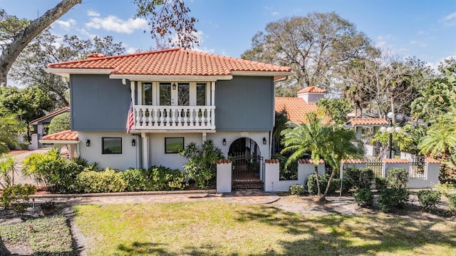 view of front of property featuring a balcony, a fenced front yard, a front lawn, and a tiled roof