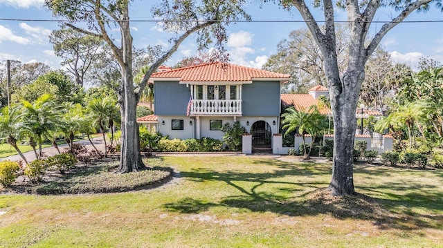 mediterranean / spanish house with a front yard, a balcony, a gate, stucco siding, and a tiled roof