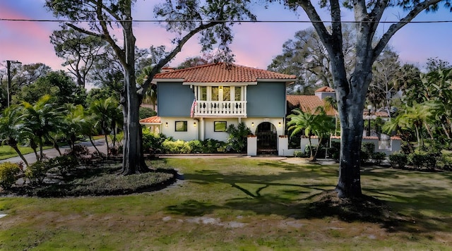 mediterranean / spanish house with a yard, stucco siding, a tiled roof, and a balcony