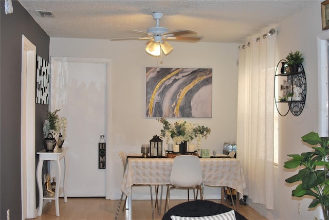 dining space with ceiling fan, a textured ceiling, and light wood-type flooring