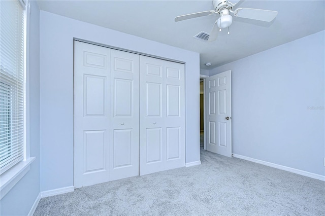 unfurnished bedroom with multiple windows, light colored carpet, ceiling fan, and a closet