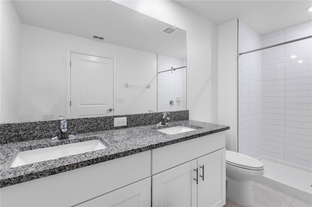 bathroom featuring vanity, toilet, tile patterned flooring, and a tile shower