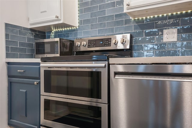 kitchen with appliances with stainless steel finishes, blue cabinetry, white cabinets, and backsplash