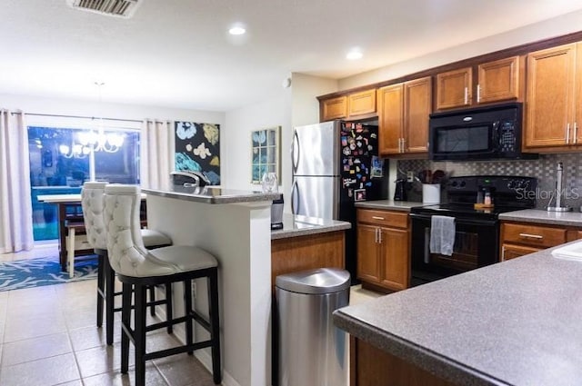 kitchen featuring pendant lighting, a breakfast bar area, backsplash, light tile patterned floors, and black appliances