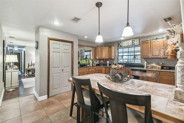 kitchen featuring light tile patterned flooring, dishwashing machine, hanging light fixtures, and backsplash