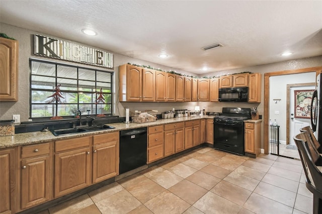 kitchen with light stone counters, sink, black appliances, and a textured ceiling