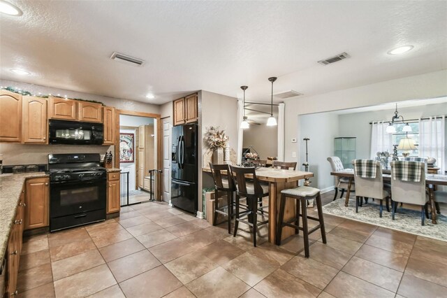 kitchen featuring tile patterned flooring, decorative light fixtures, black appliances, and a kitchen breakfast bar