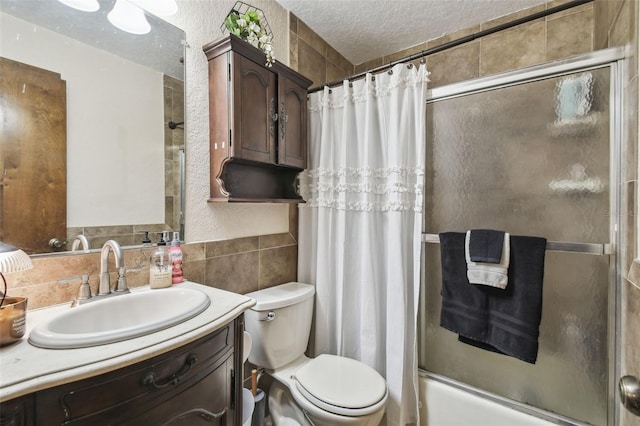 full bathroom featuring shower / bath combination with glass door, tile walls, vanity, a textured ceiling, and toilet