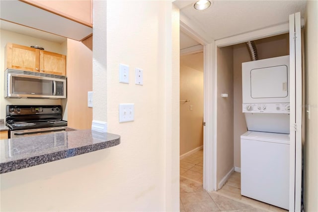 clothes washing area featuring stacked washing maching and dryer and light tile patterned flooring